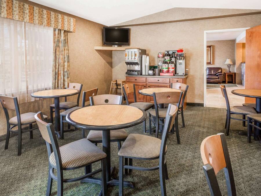 A hotel room with a dining area featuring round tables and chairs, a coffee machine, and a television on a shelf.