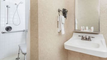 Une salle de bain avec un lavabo blanc, un miroir et un espace douche équipé d’une barre d’appui.