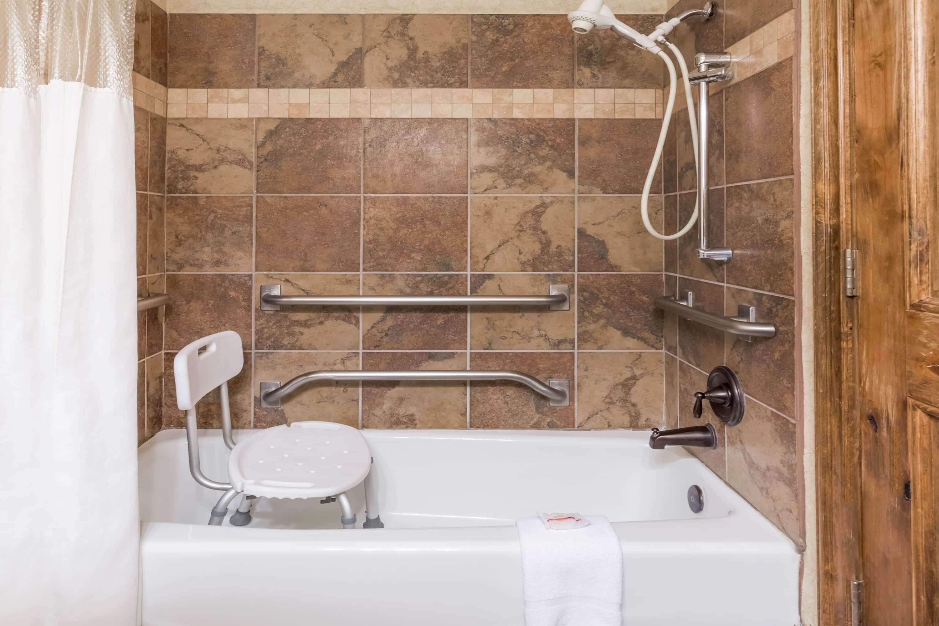 A bathroom with a bathtub, grab bars, a showerhead, and a towel rack.