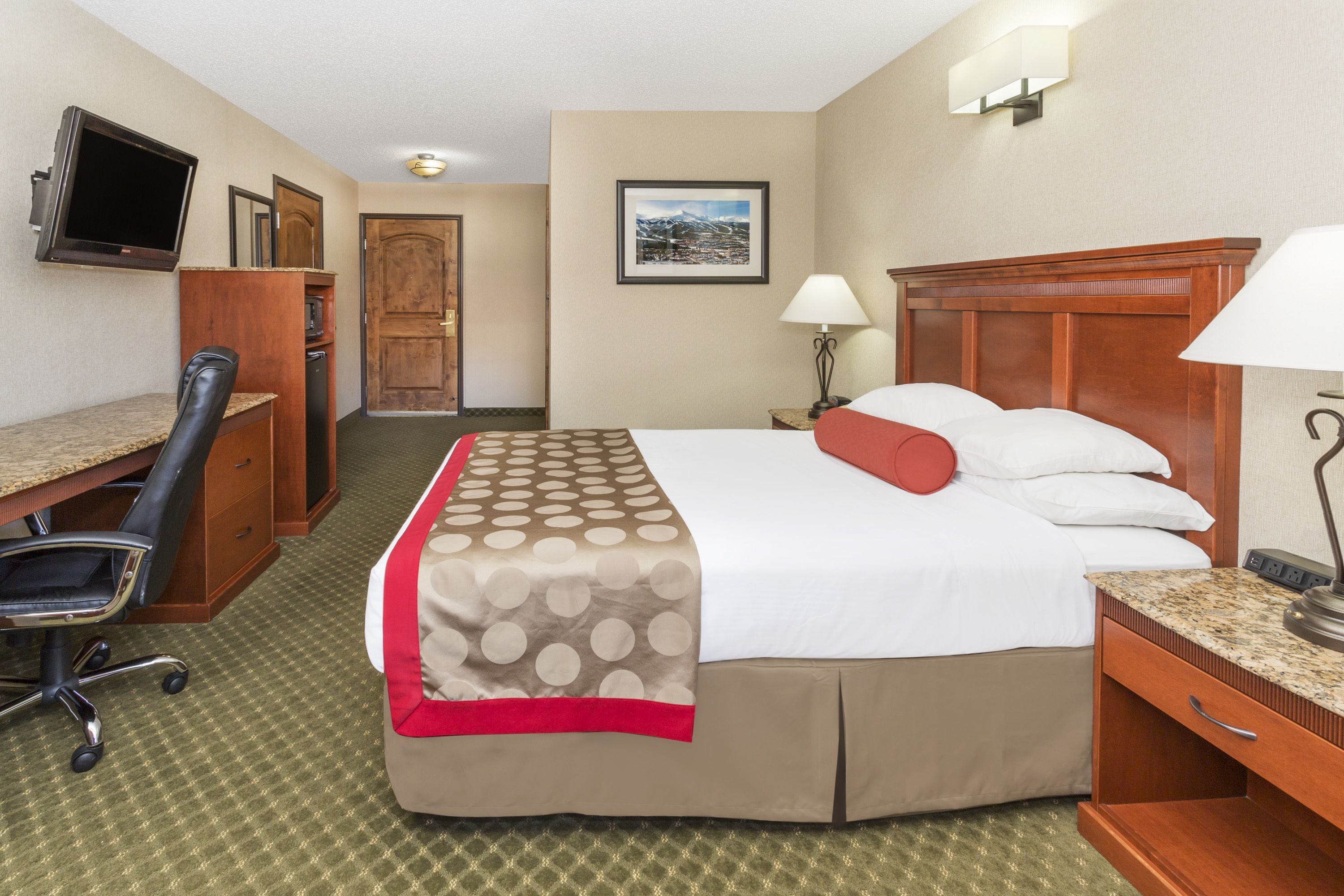 A hotel room with a bed, desk, chair, TV, and a picture on the wall.