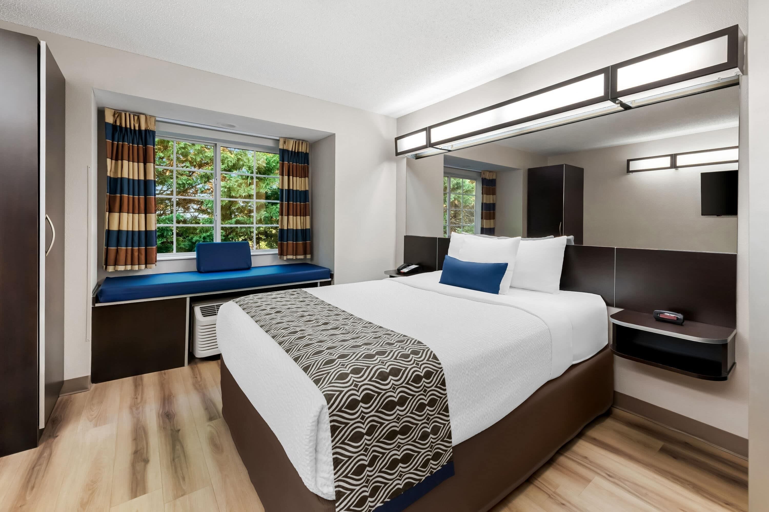 Une chambre d’hôtel moderne dotée d’un grand lit, d’une table de chevet, d’une fenêtre avec des rideaux, d’une banquette intégrée et d’un téléviseur.