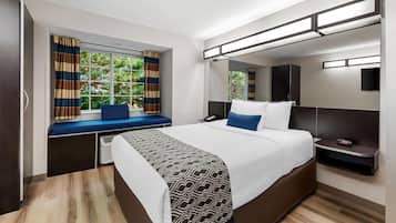 Une chambre d’hôtel moderne dotée d’un grand lit, d’une table de chevet, d’une fenêtre avec des rideaux, d’une banquette intégrée et d’un téléviseur.