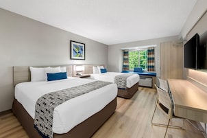 Habitación de hotel con dos camas, un escritorio, un televisor y una ventana con cortinas.