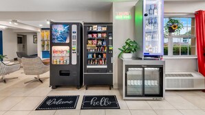 A modern hotel lobby with vending machines, a refrigerator, a glass door, and a 'Liquor Beer Wine' sign. - Microtel Inn & Suites by Wyndham Greenville / Woodruff Rd (Greenville)