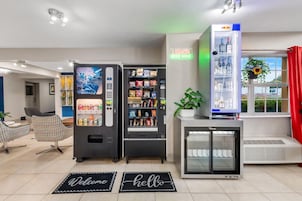 Un moderno vestíbulo de hotel con máquinas expendedoras, un refrigerador, una puerta de vidrio y un letrero que dice 'Licores, Cerveza, Vino'.