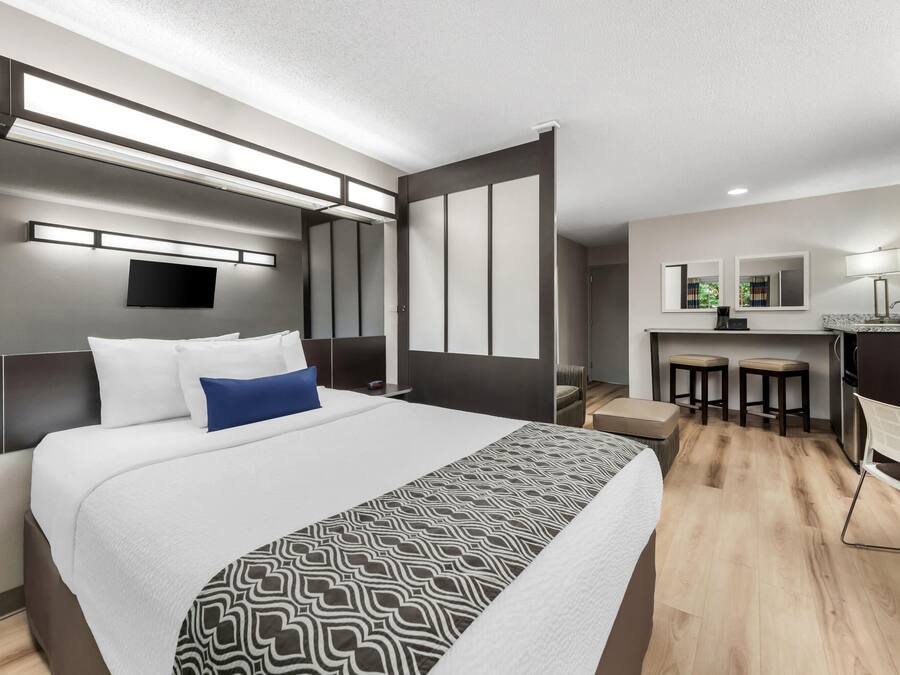 A modern hotel room with a large bed, a desk, and a kitchenette.