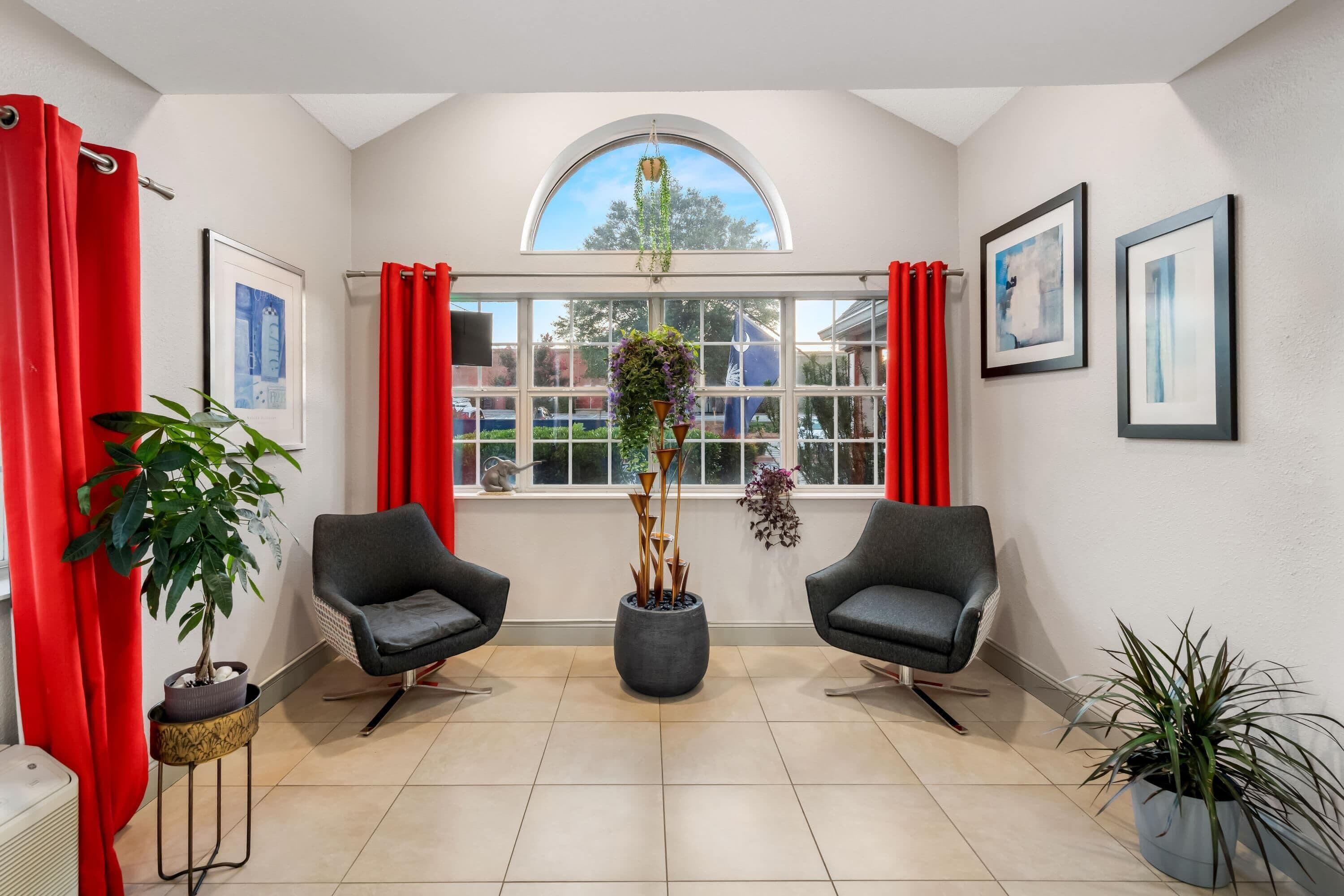 Una habitación con dos sillones, un ventanal con cortinas, una planta en maceta y cuadros en las paredes.