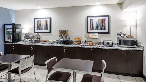 A modern kitchen with a granite countertop, a built-in grill, a microwave, and a coffee maker. There are two framed artworks on the wall and a refrigerator with a built-in ice maker. - Microtel Inn & Suites by Wyndham Greenville / Woodruff Rd (Greenville)