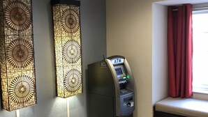 A room with a wall-mounted ATM, decorative wall panels, a window with red curtains, and a tiled floor. - Microtel Inn & Suites by Wyndham Greenville / Woodruff Rd (Greenville)