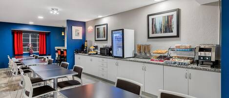 Un comedor moderno con mesas y sillas, un refrigerador, microondas y cafetera.