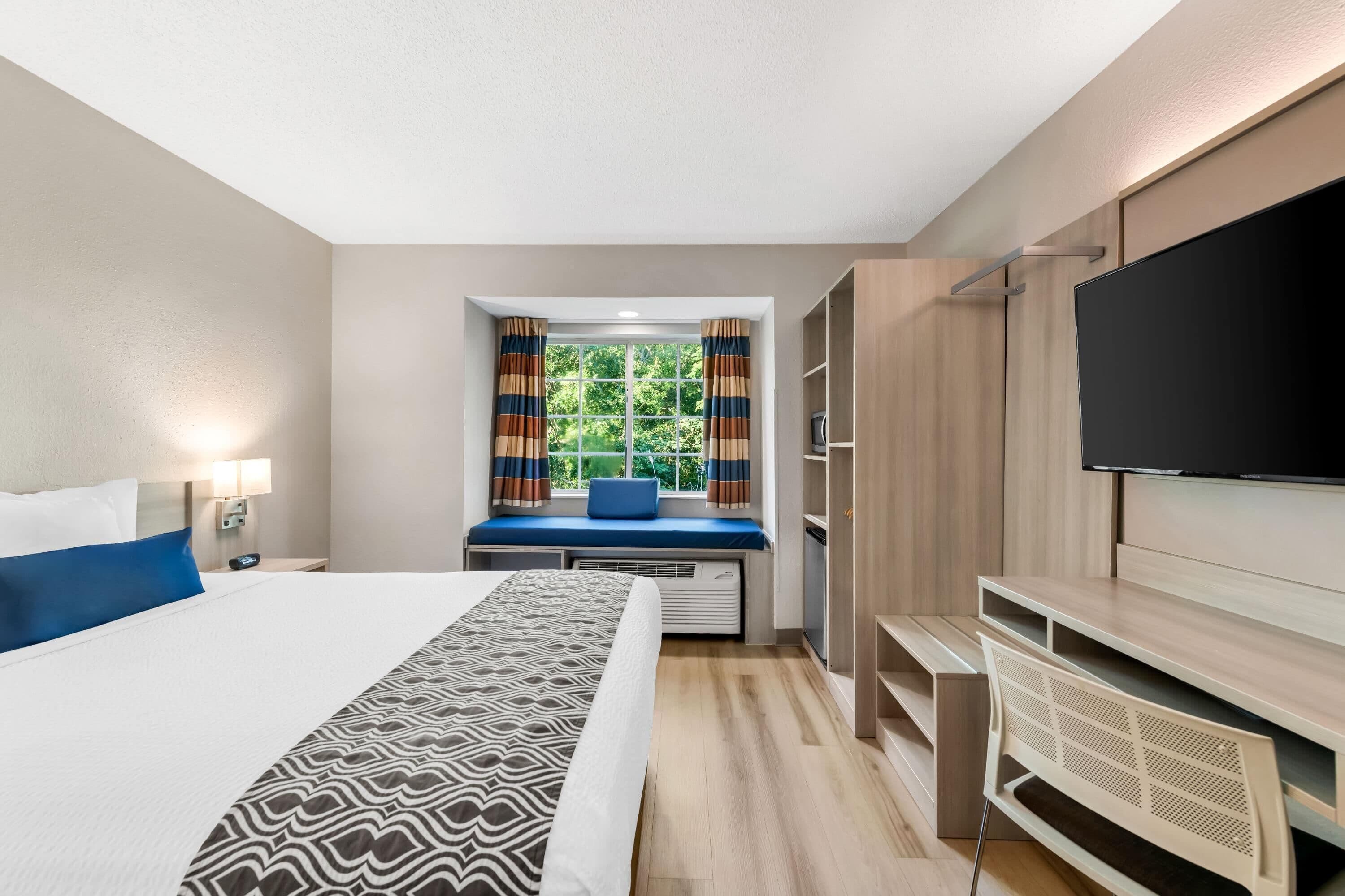 A hotel room with a bed, a television, a window with curtains, and a wardrobe.