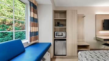 Habitación de hotel moderna con sofá azul, microondas, mini refrigerador y TV montada en la pared.
