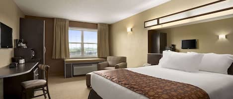 A hotel room with a bed, desk, chair, TV, and a window with curtains.