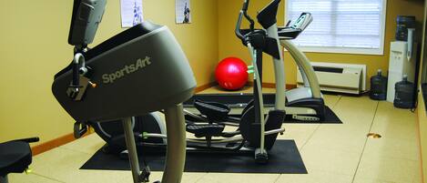 Un gimnasio con bicicletas estáticas, cintas de correr y una pelota de ejercicios roja.