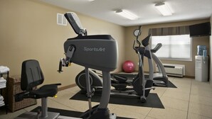 A gym with exercise equipment, a wall clock, and a window with blinds. - Microtel Inn By Wyndham Mineral Wells/Parkersburg (Mineralwells)