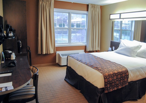 A hotel room with a bed, a desk with a coffee maker, a chair, and a window with curtains.