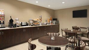 A hotel dining area with a buffet setup, multiple tables, and chairs. - Microtel Inn By Wyndham Mineral Wells/Parkersburg (Mineralwells)