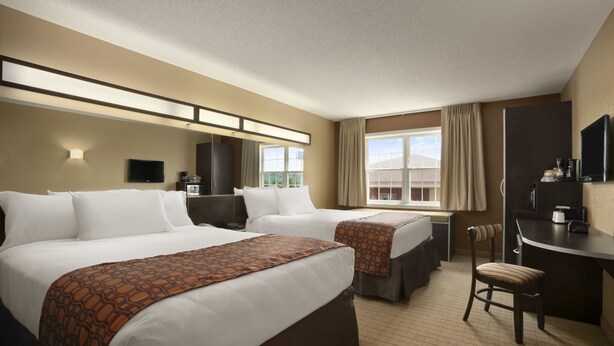A hotel room with two beds, a desk, a chair, a television, and a window with curtains. - Microtel Inn By Wyndham Mineral Wells/Parkersburg (Mineralwells)
