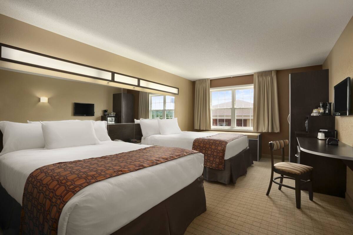 A hotel room with two beds, a desk, a chair, a television, and a window with curtains.