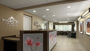 A reception area with a counter displaying floral artwork, a sign for 'MICROTEL INN BY WYNDHAM', and a view into a dining area with tables and chairs. - Microtel Inn By Wyndham Mineral Wells/Parkersburg (Mineralwells)