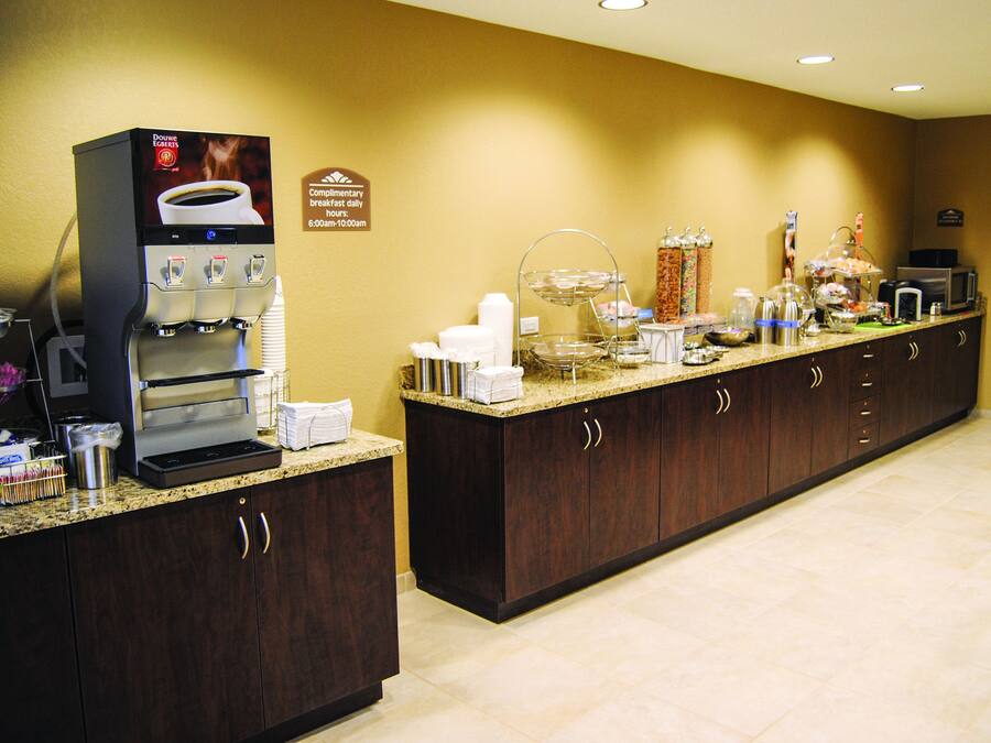 A hotel breakfast area with a coffee machine, tea station, and various food items on a counter.