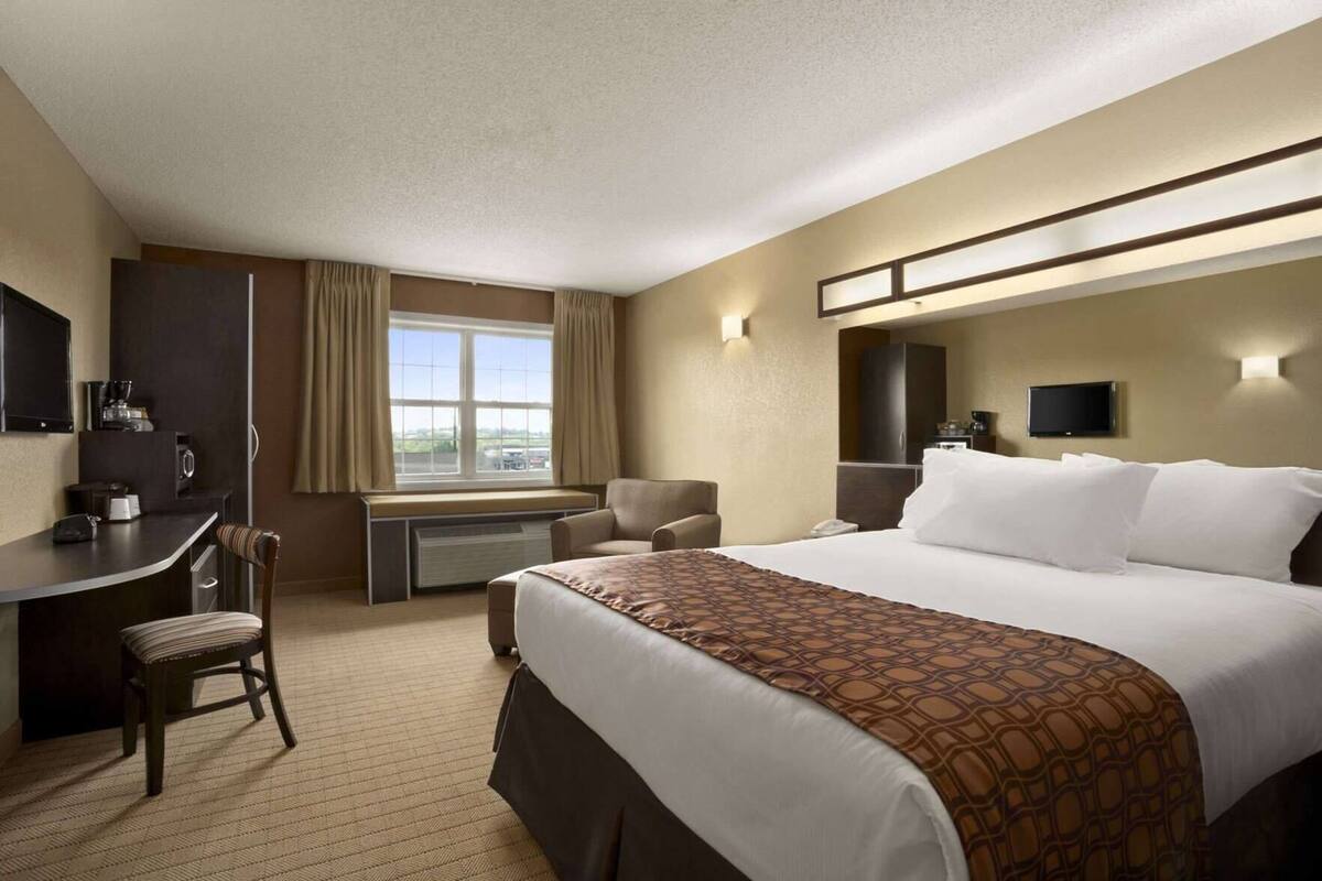 A hotel room with a bed, desk, chair, and a television.