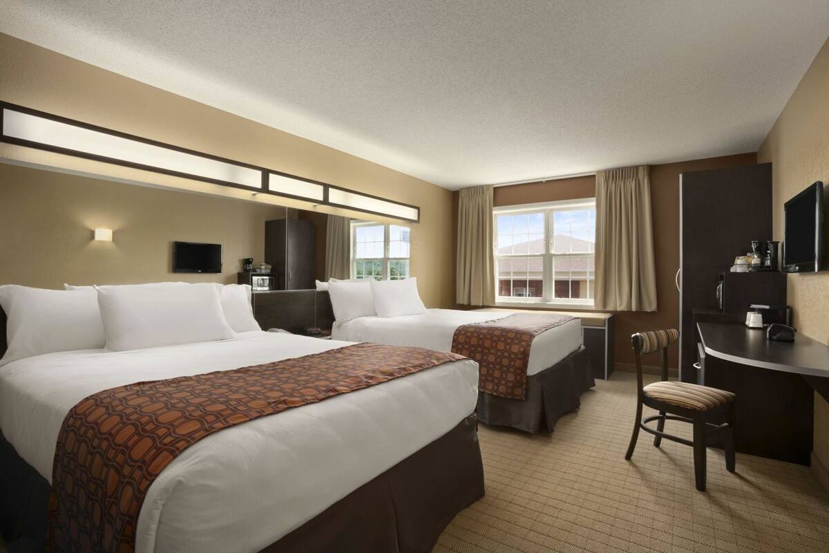 A hotel room with two beds, a desk, a chair, a TV, and a window with curtains.