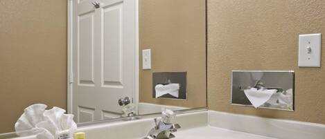 A bathroom with a white sink, a mirror, and a towel dispenser.