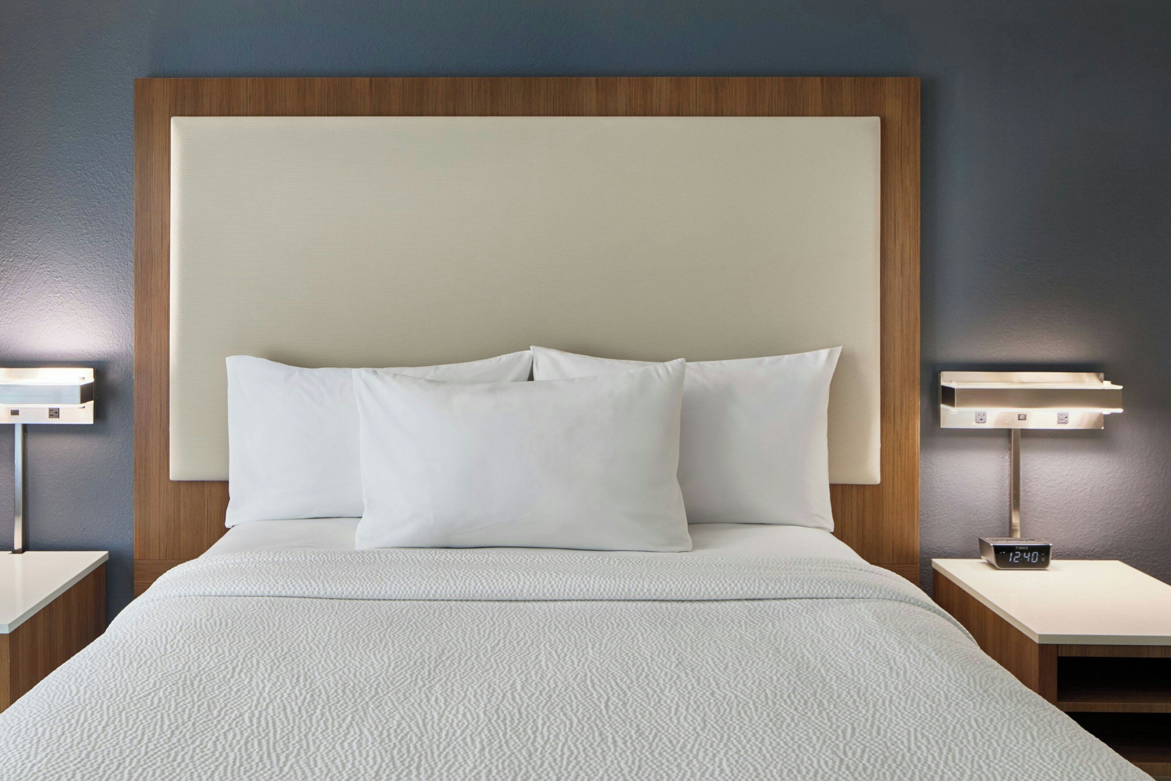 A neatly made bed with a headboard, two bedside tables, and a nightstand with a clock.