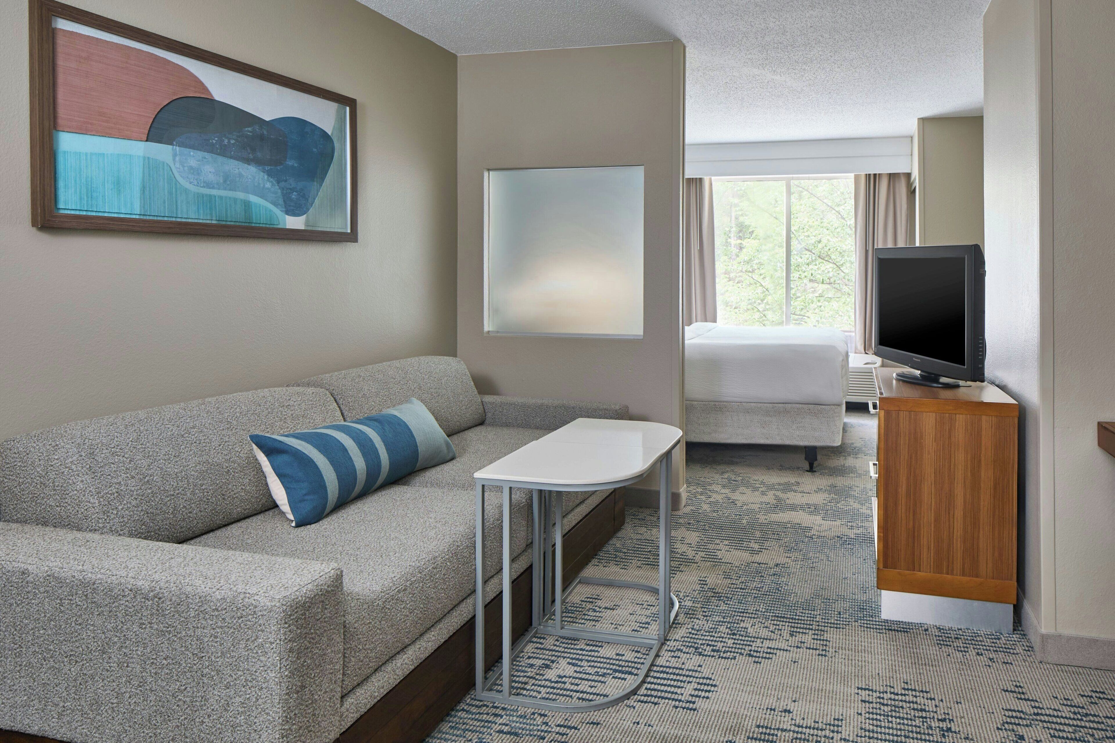 A hotel room with a sofa, a small table, a TV, and a window with a view.