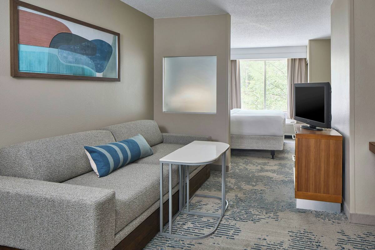 Ein Hotelzimmer mit einer Sitzecke, einem kleinen Tisch, einem Fernseher und einem Fenster mit Blick.