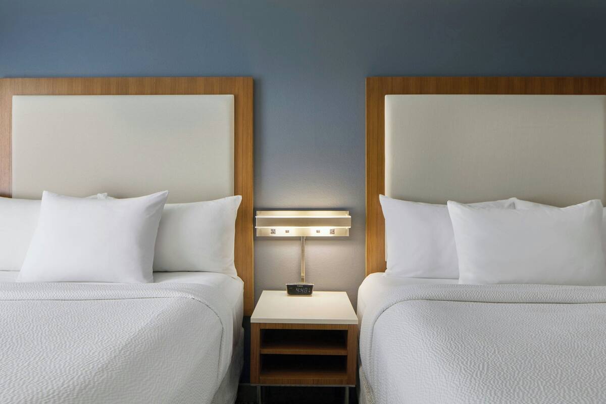 Ein Hotelzimmer mit zwei Betten, einem Nachttisch mit einer Uhr und einer Wandleuchte.