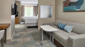 Una camera d'albergo con un letto, un divano, un tavolino, una TV e un quadro appeso al muro.