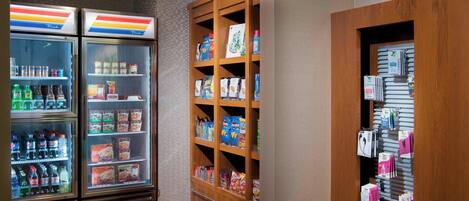Un vestíbulo de hotel con dos dispensadores de bebidas refrigeradas, un expositor de aperitivos y alimentos, y una máquina expendedora.