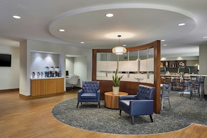 A modern lobby with a round seating area, a reception desk, and a dining area.