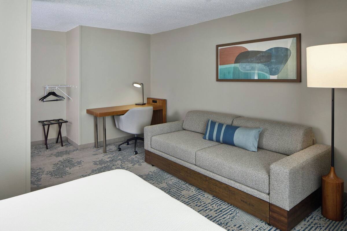 Ein Hotelzimmer mit Bett, einer Couch, Schreibtisch, Stuhl, Lampe und einem Wandbild.