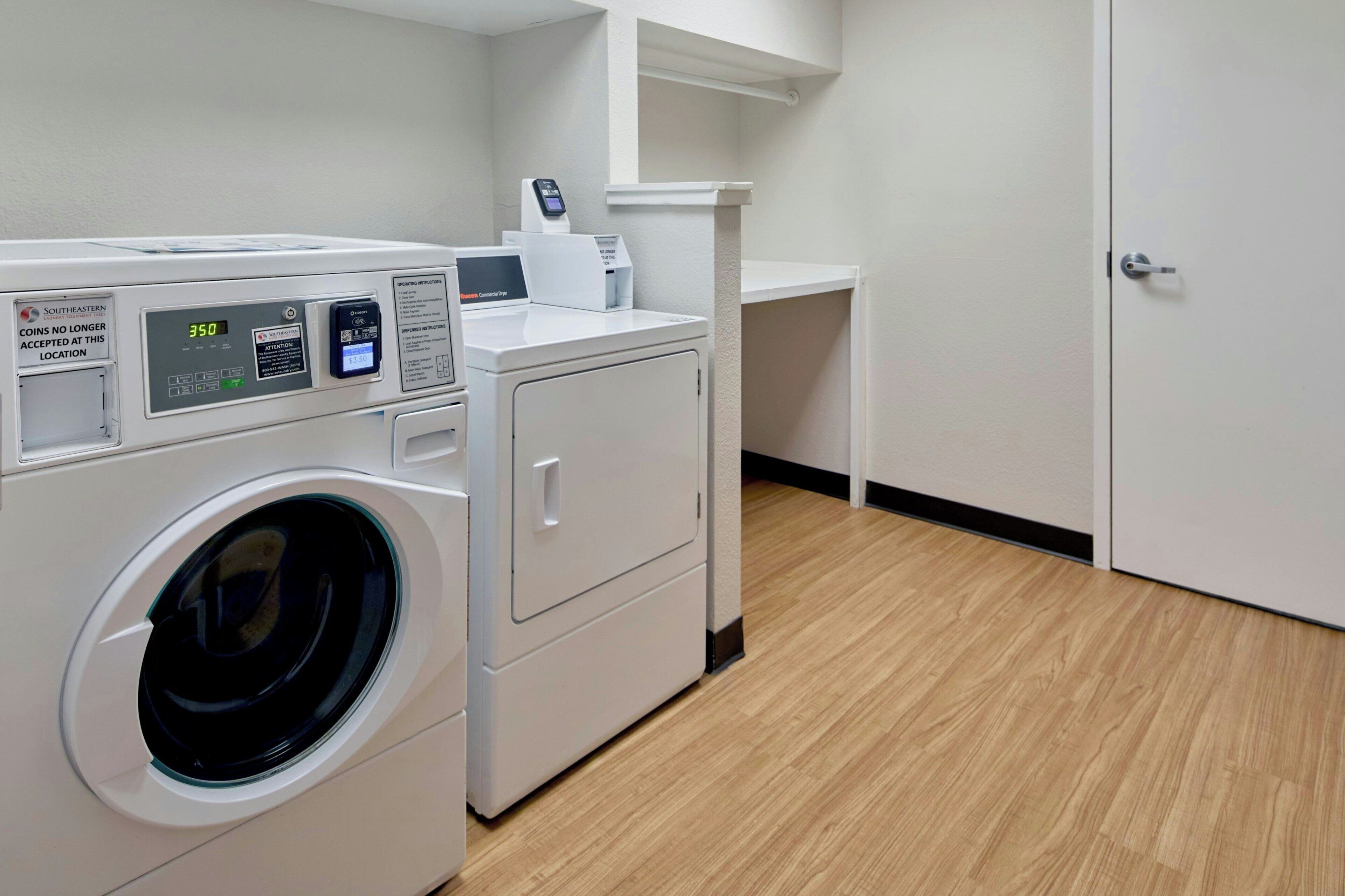 Een wasruimte met een voorlader wasmachine en droger, een digitaal bedieningspaneel en een machine op muntbasis.
