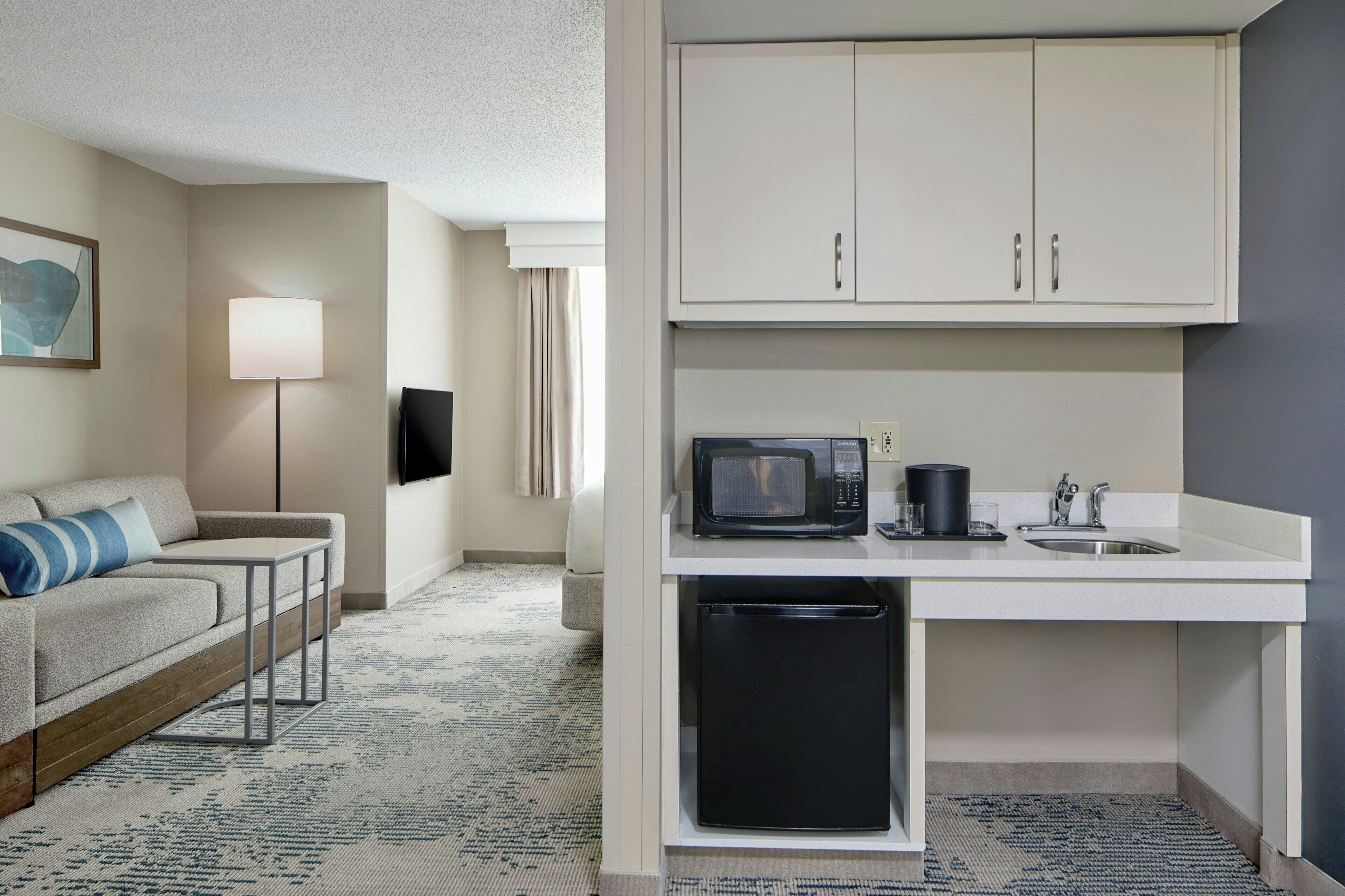 Una habitación de hotel compacta con kitchenette, un sofá, una lámpara y un televisor de pantalla plana.