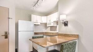 Una cocina compacta con gabinetes blancos, microondas, refrigerador y un pequeño comedor con banco.