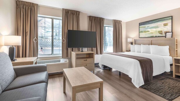 Habitación de hotel con cama, televisión, escritorio, silla y un amplio ventanal con cortinas.