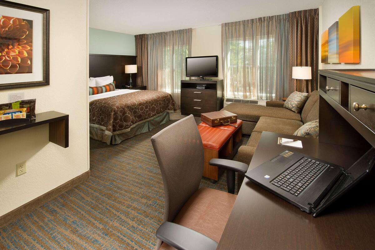 Een hotelkamer met een bed, een bank, een bureau met een laptop, een televisie en een tafeltje met een lamp.