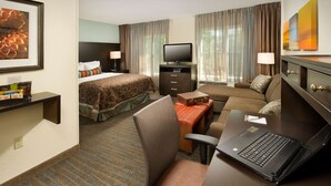 Une chambre d’hôtel comprenant un lit, un canapé, un bureau avec un ordinateur portable, une télévision et une petite table avec une lampe.