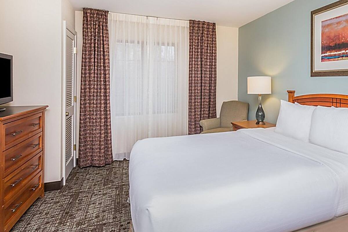 Een hotelkamer met een groot bed, een houten dressoir, een bureau met lamp, een stoel en een televisie.