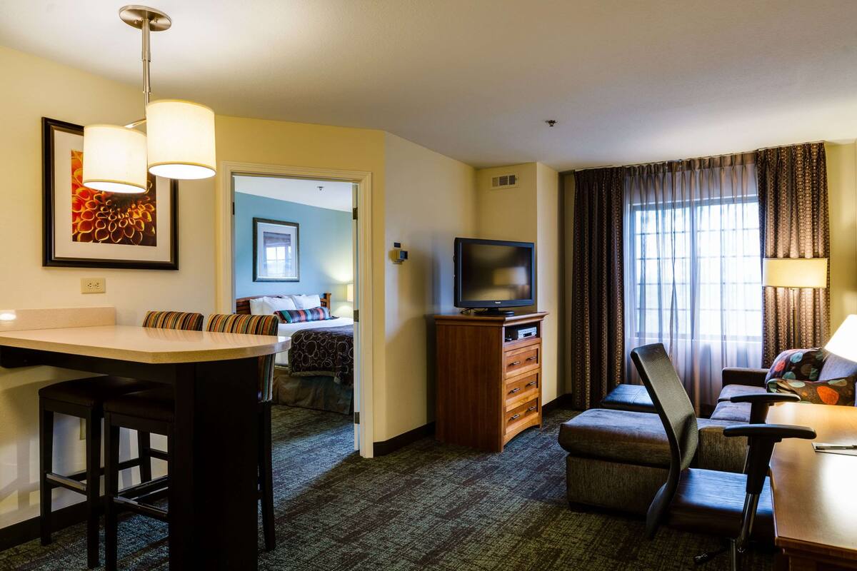 Een hotelkamer met een kitchenette, een televisie, een bank en een bed.