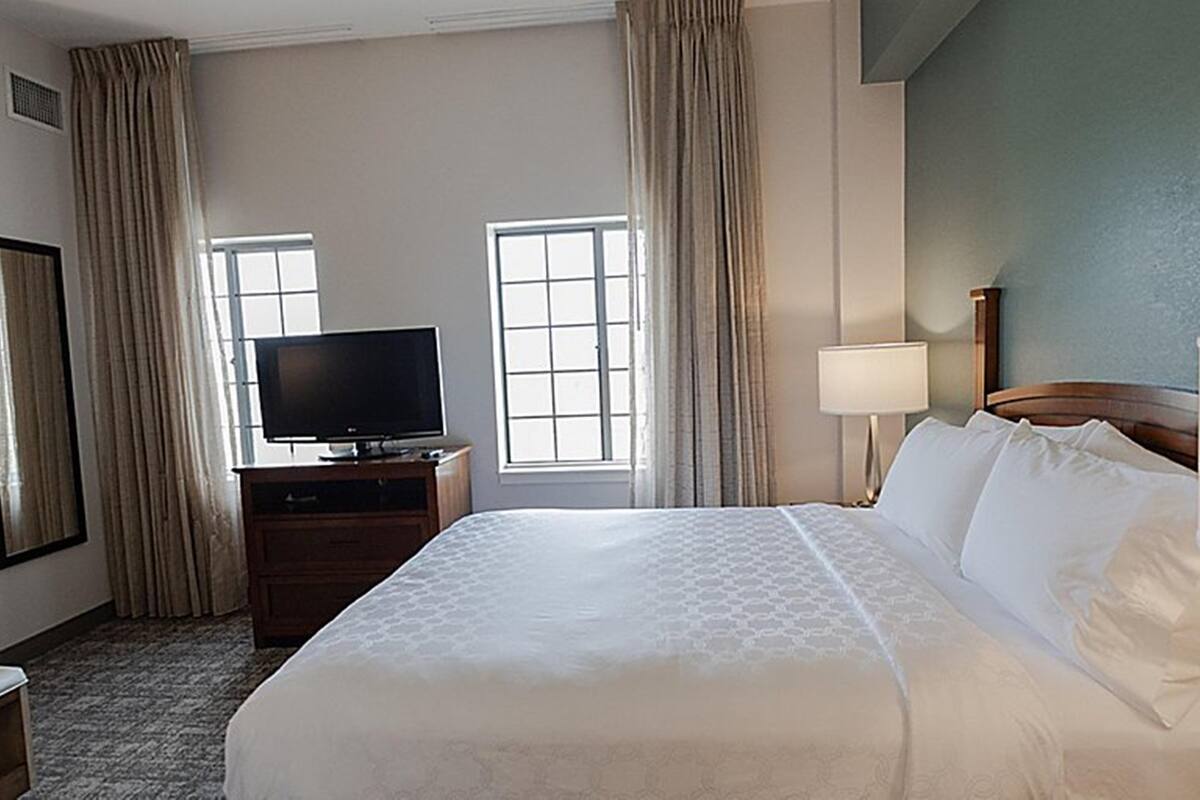 Een hotelkamer met een groot bed, een televisie op een houten kast en twee ramen met gordijnen.