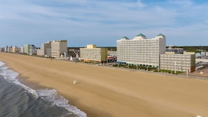 Un hotel frente a la playa con varias edificaciones, una playa de arena y olas del océano.