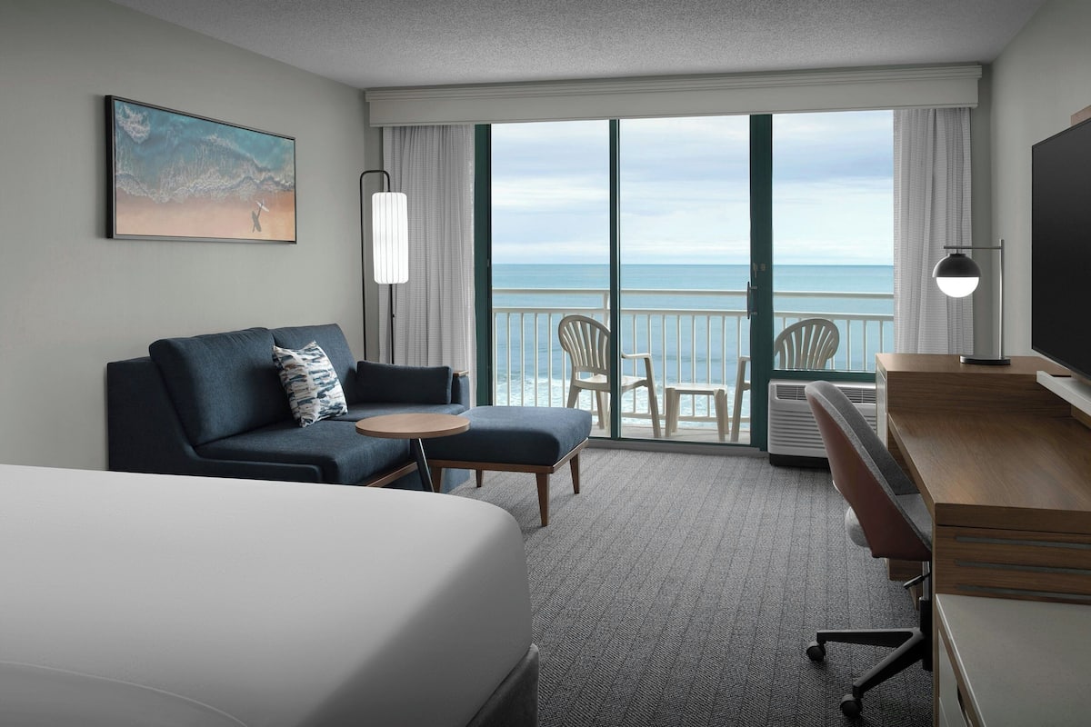 A hotel room with a bed, a sofa, a desk, and a view of the ocean.
