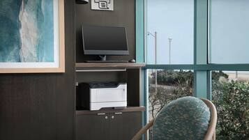 Een werkplek met een computer, printer en uitzicht op het groen door grote ramen.