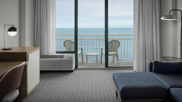 Habitación de hotel con balcón, escritorio, silla, cama y vistas al mar.