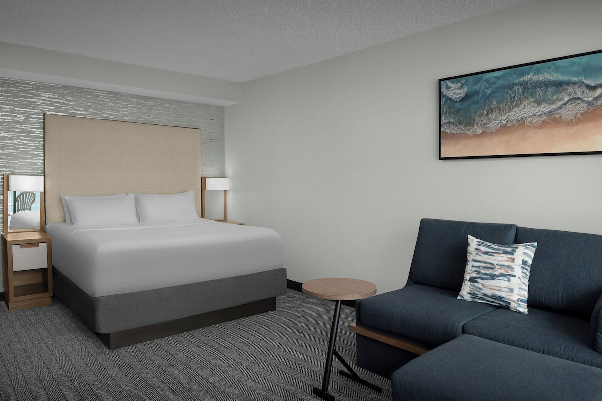 A hotel room with a bed, a sofa, a small table, and a painting on the wall.